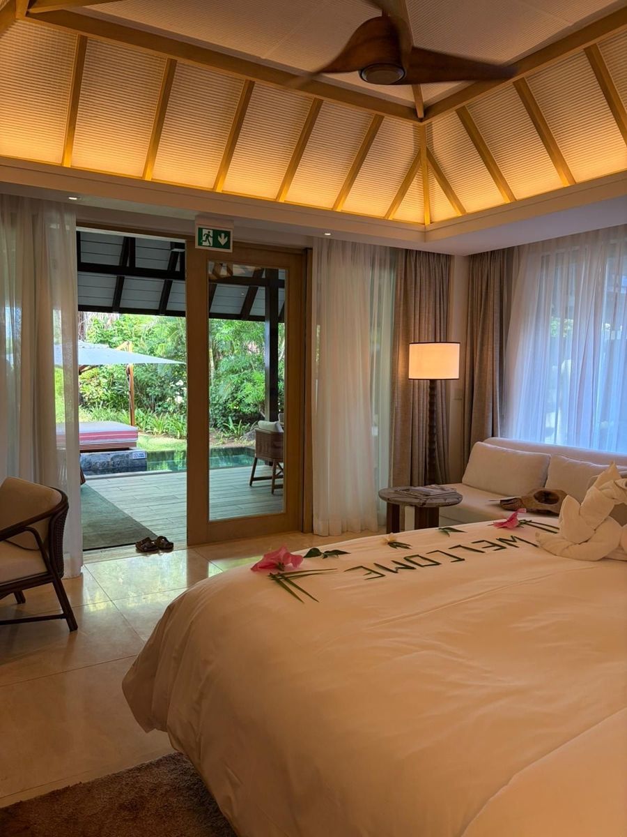 Villa bedroom with high pitched ceiling, sliding doors open onto a terrace and plunge pool, and rose petals spelling welcome on the bed, Four Seasons Mauritius at Anahita