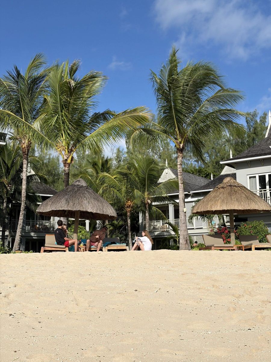Beach with palm-thatched parasols, sunloungers and lounging guests fronting the St Regis villas, Mauritius at Le Morne