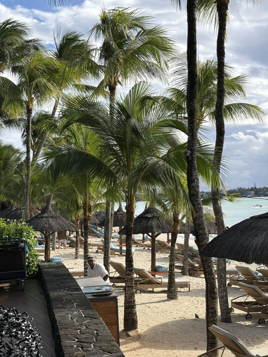 Palm-lined beach frontage at Beachcomber Royal Palm with thatched parasols, sunloungers and the ocean beyond, Mauritius