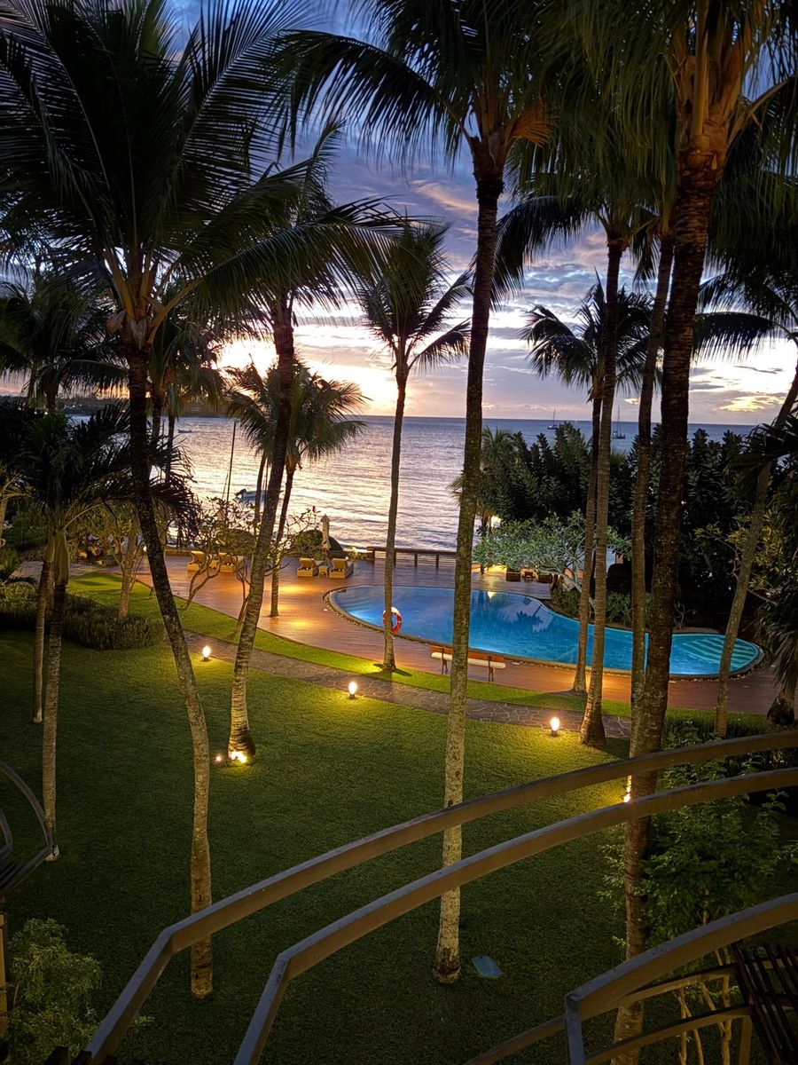 Sunset over the lit pool and ocean, framed by palms, at Beachcomber Royal Palm, Mauritius