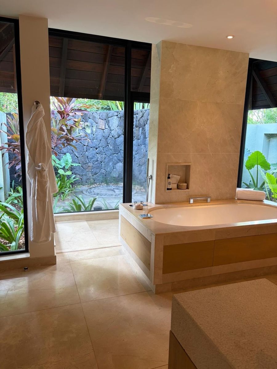 Villa bathroom at Four Seasons Mauritius at Anahita, with a deep marble tub, robe and floor-to-ceiling windows onto a private garden