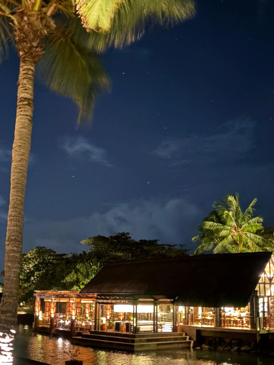 Awase restaurant lit up at night under a starlit sky, framed by palms, Four Seasons Mauritius at Anahita